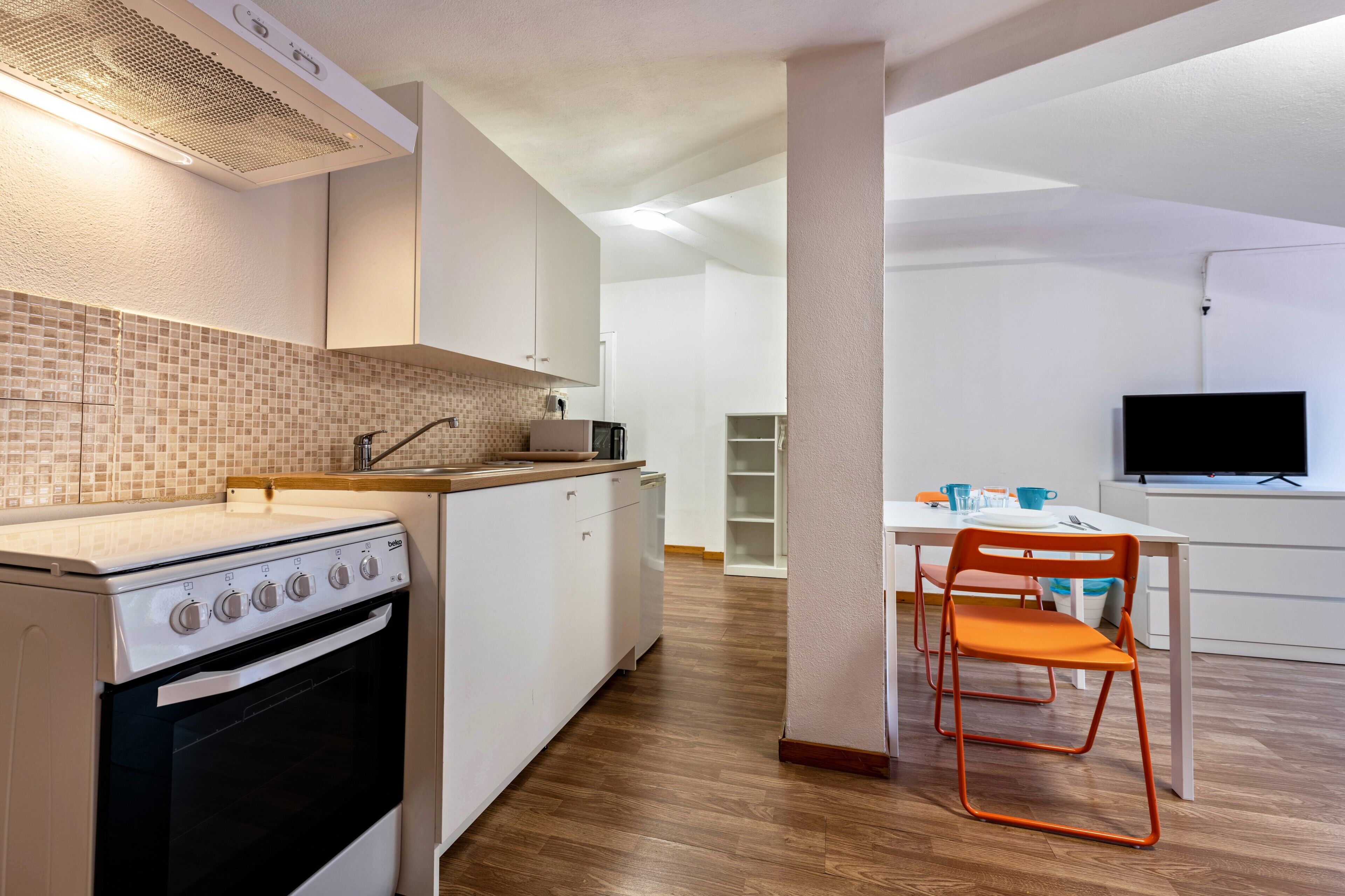 A modern kitchen with white cabinets, a stove, and a dining area with a table and chairs.