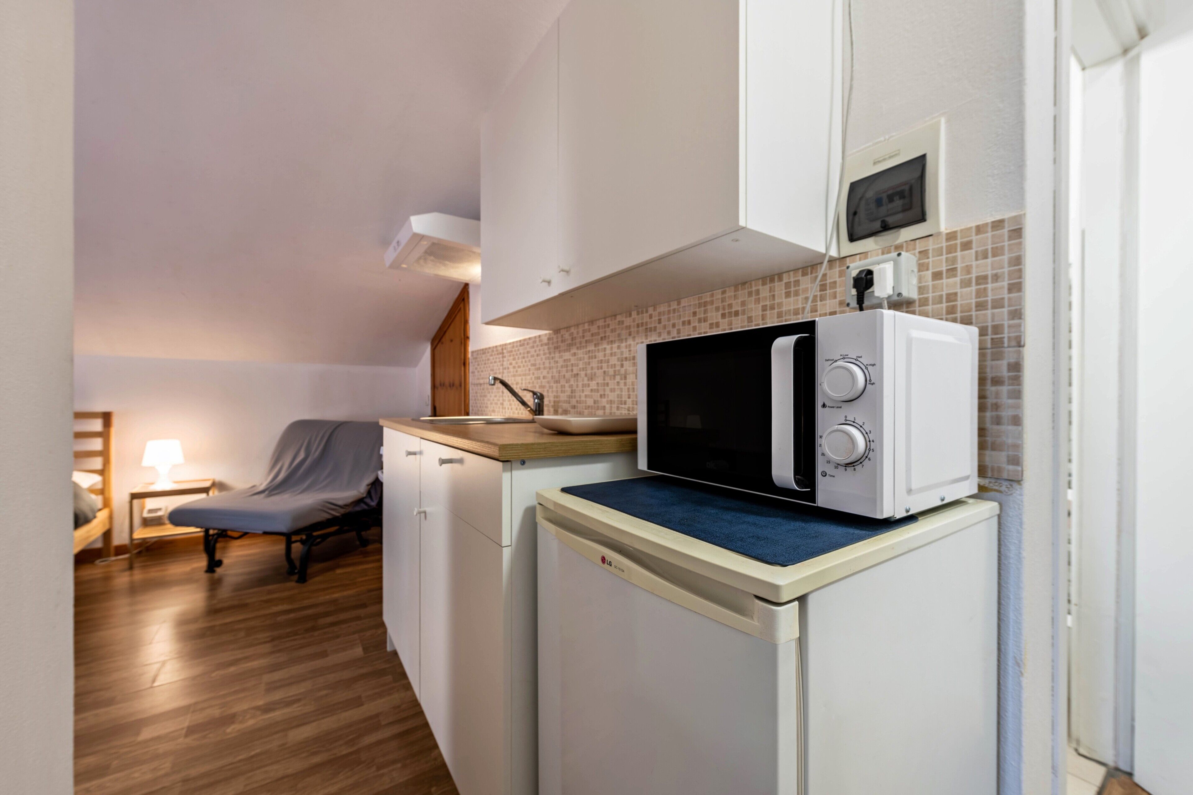 A compact kitchenette with a microwave, a small sink, and a chair.