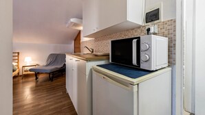 Una kitchenette compacta con microondas, un lavamanos pequeño y una silla.
