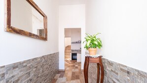 Un pasillo con suelo de baldosas, un espejo con marco de madera y una planta en maceta sobre un pedestal de madera.