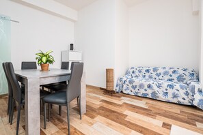 A modern living room with a dining table, chairs, a sofa, a potted plant, and a small side table.