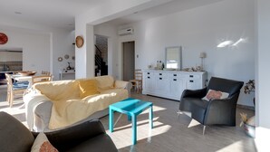 A spacious living area with a sofa, a coffee table, and a chair. There is a kitchen area with cabinets and a dining table. - Villa "Domus Bianca" with Sea View, Garden & Wi-Fi (San Giovanni di Sinis)