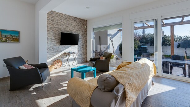 A modern living room with a stone wall, a flat-screen TV, a sofa, and a dining area with a table and chairs. - Villa "Domus Bianca" with Sea View, Garden & Wi-Fi (San Giovanni di Sinis)