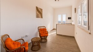 A room with wicker chairs, a small round table, a kitchen area, and a view through a window. - Villa "Domus Bianca" with Sea View, Garden & Wi-Fi (San Giovanni di Sinis)