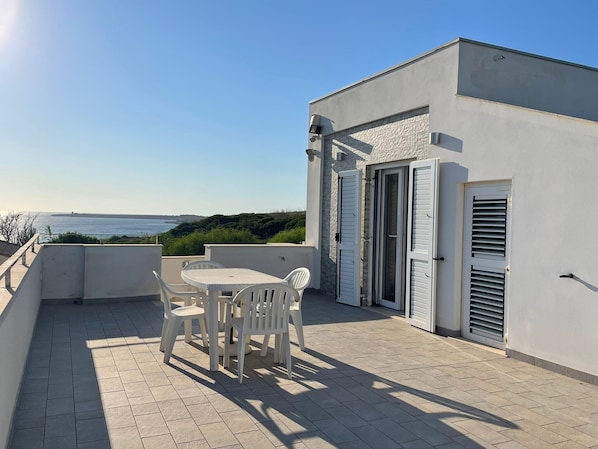 A rooftop terrace with a table and chairs, a door, and a view of the sea.