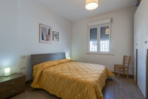 A bedroom with a bed, a chair, a nightstand, a lamp, and a window with blinds.