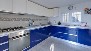 A modern kitchen with white and blue cabinets, a gas stove, and a window with a view. - Villa "Domus Bianca" with Sea View, Garden & Wi-Fi (San Giovanni di Sinis)