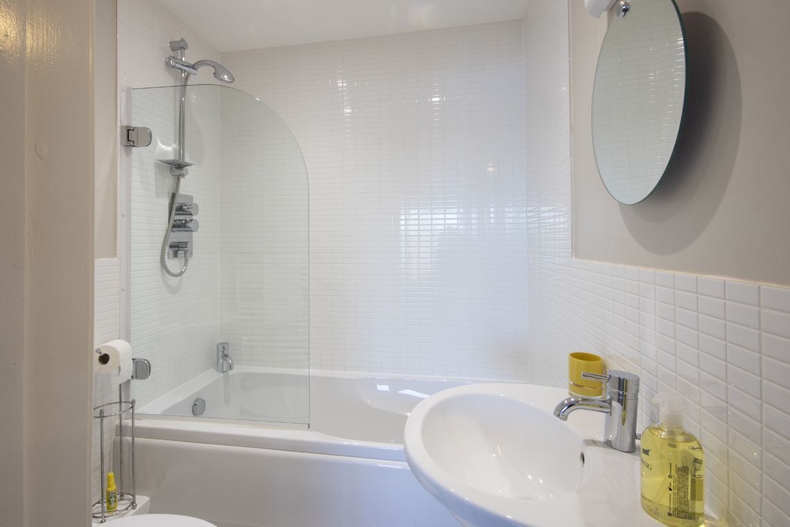 Un bagno moderno con doccia vetrata, una vasca da bagno bianca, un lavandino con specchio e articoli da toilette sul ripiano.