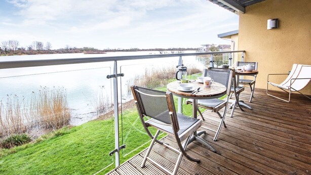 A deck with a table and chairs overlooking a lake. - Clearwater 31, The Lakehouse - Waterside Holiday Cottage, Spa Access, Sleeps 8 (Somerford Keynes)