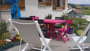 A patio with a table and chairs, a blue umbrella, and a view of a house in the background. - Fully-equipped Meublé de Tourisme for rent, sleeps 6 (Discounts + nights) (nanchez)