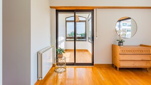 Ein Zimmer mit Holzboden, einer Schiebetür zum Balkon und einem Holzkasten sowie einem runden Spiegel an der Wand.