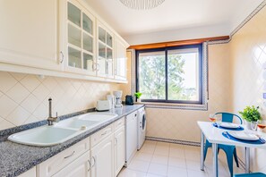 Eine kompakte Küche mit Spüle, Arbeitsplatte, Schränken, einem Fenster und einem Essbereich mit Tisch und Stühlen.