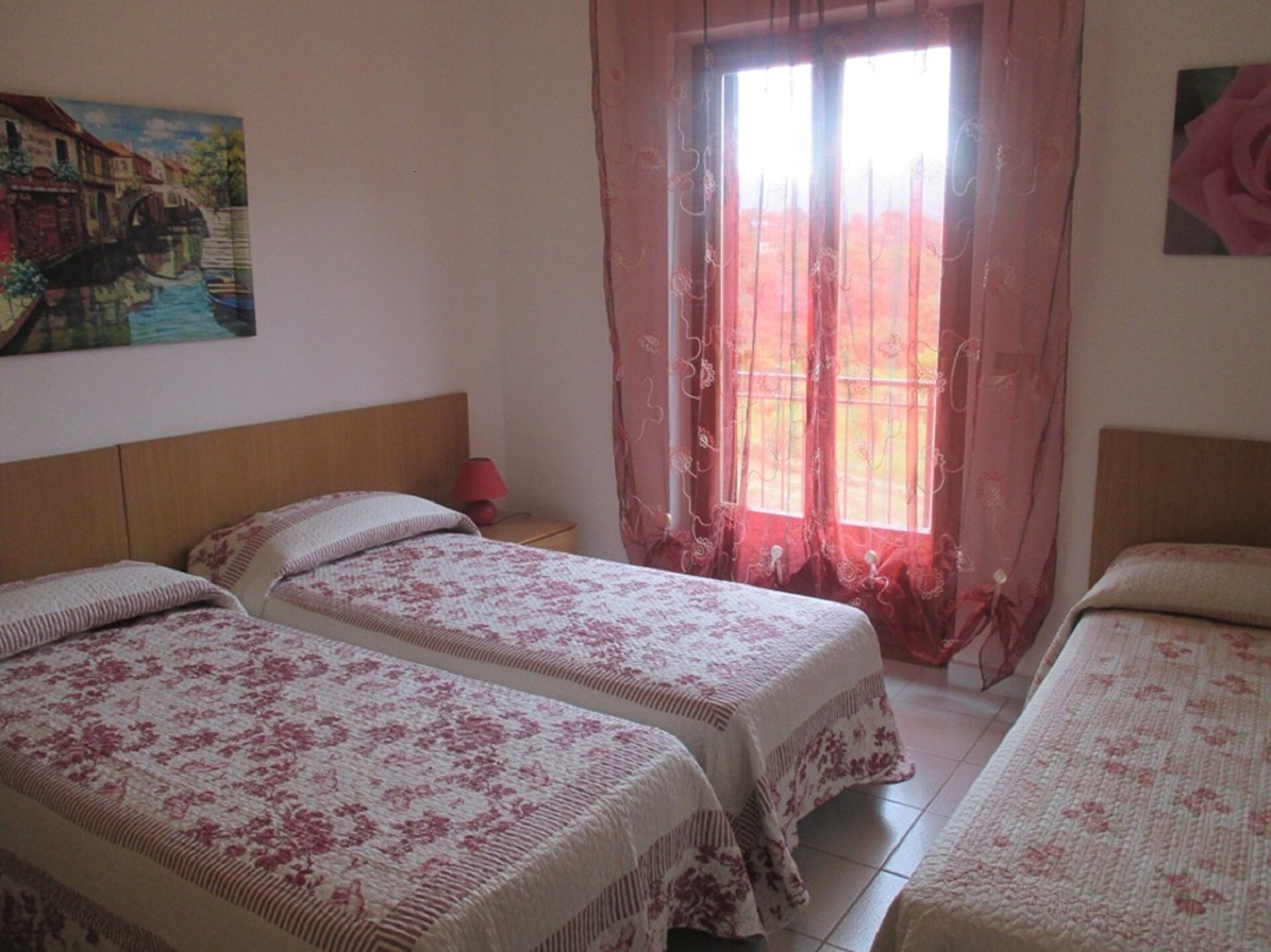 A bedroom with two beds, a nightstand, a lamp, and a window with curtains.