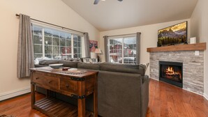 Een woonkamer met een open haard, een bank, een salontafel en een tv boven de open haard.