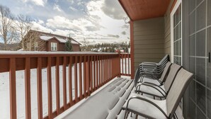 Een overdekt terras met houten leuning en meerdere stoelen, met uitzicht op een besneeuwd landschap met huizen en bomen.