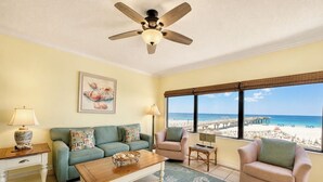 A living room with a view of the beach, a ceiling fan, a sofa, a coffee table, and a chair. - Private Fishing Pier! (Orange Beach)