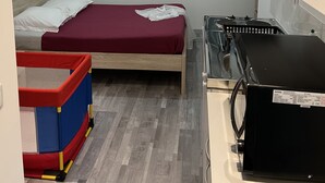 Une chambre de taille modeste, comprenant deux lits, une petite kitchenette, une fenêtre avec des rideaux légers et un parc pour enfants.