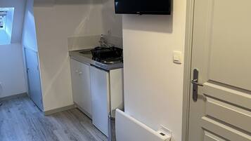 Habitación compacta con kitchenette, cama con cubierta roja y televisor montado en la pared.