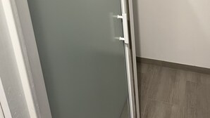 Une pièce avec une porte de douche en verre, des murs blancs et un plancher en bois.