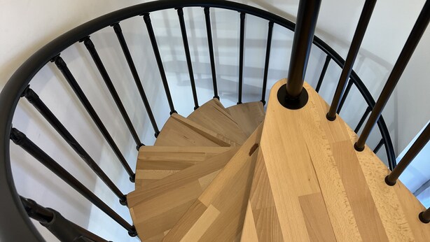 Un escalier en colimaçon avec des rampes en métal noir et des marches en bois.