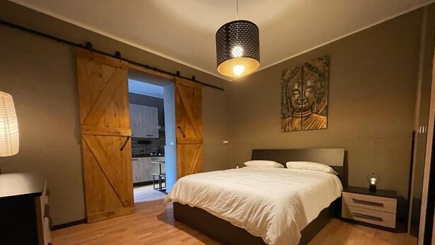 Une chambre avec un grand lit, un plancher en bois, une porte coulissante de style grange, une lampe fixée au mur et une statue de Bouddha.