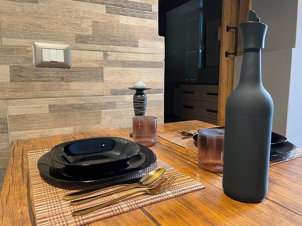 Une table à manger avec une assiette noire, des couverts et un vase foncé.
