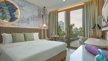 Camera d'albergo con un letto grande, un tavolino con una lampada, un tappetino da yoga e vista sulla città attraverso un'ampia porta scorrevole in vetro.