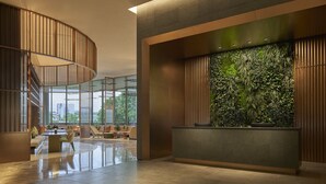 Un vestíbulo moderno con una escalera curva, un mostrador de recepción con pared verde y un área de descanso con sofás y sillones.