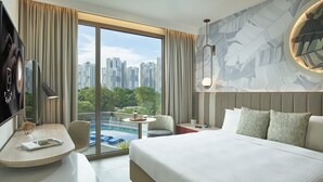 Una habitación de hotel moderna con una cama grande, un escritorio con una computadora portátil, una silla, una mesita con una bebida y vistas a la silueta urbana a través de amplios ventanales.