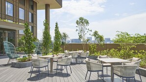 Un patio al aire libre con varias mesas y sillas, rodeado de vegetación y vistas a un paisaje urbano.