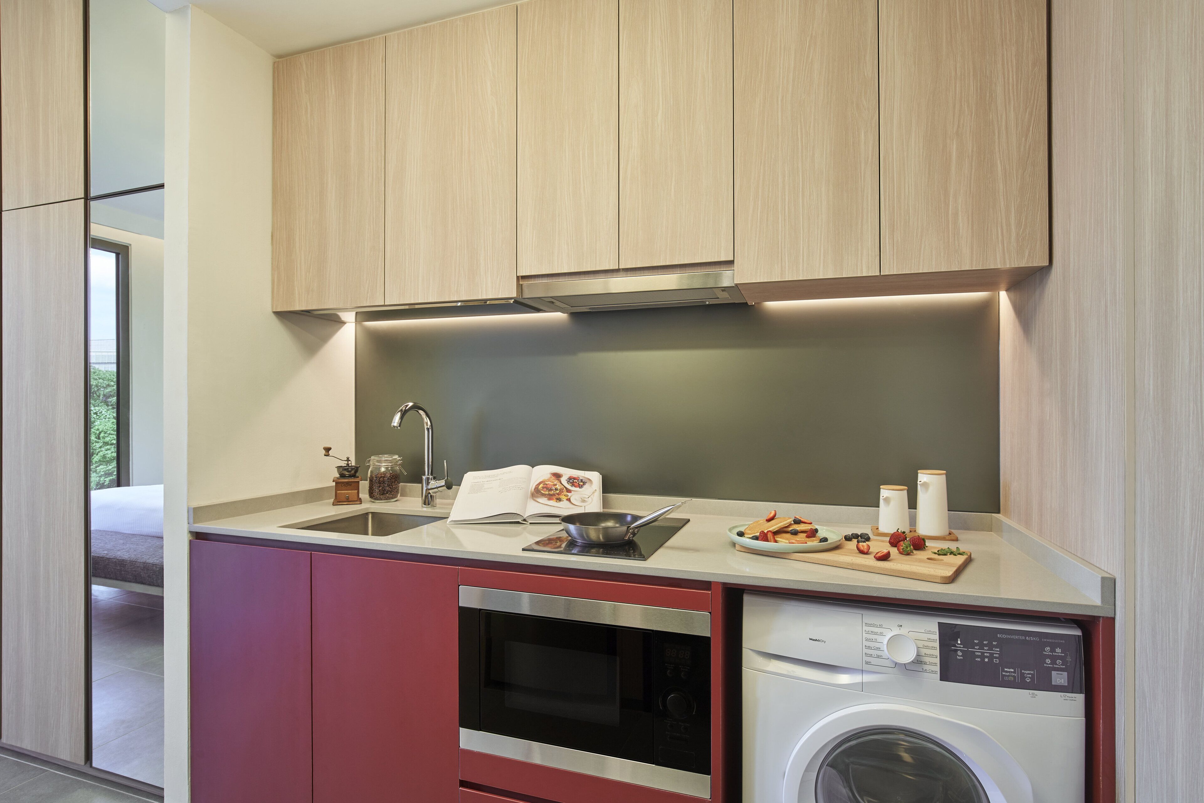 Una cocina moderna con armarios de madera, horno de acero inoxidable, lavadora integrada y encimera con tabla de cortar y utensilios.