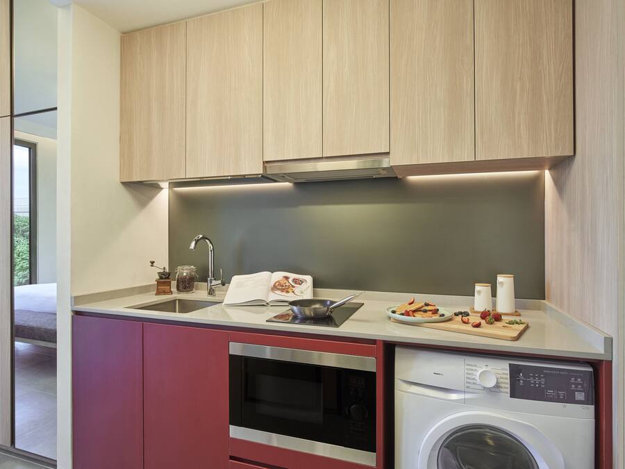 A modern kitchen with wooden cabinets, a stainless steel oven, a built-in washing machine, and a countertop with a cutting board and utensils.