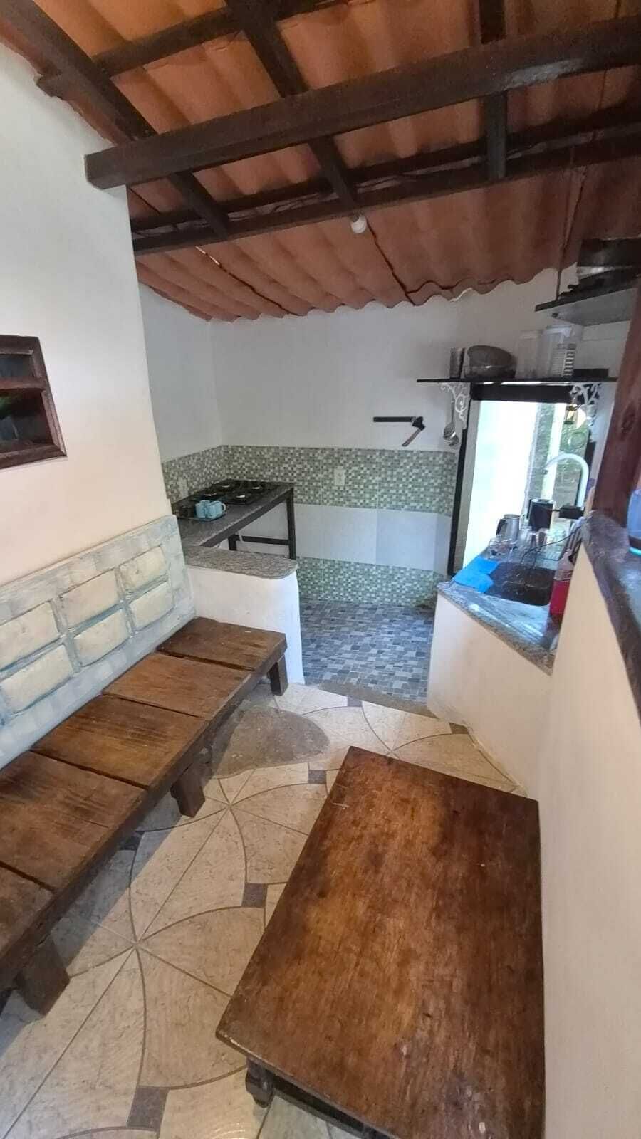A small kitchen with a tiled backsplash, a gas stove, and a sink. There is a wooden bench and a small table.