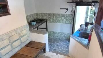 A small kitchen with a tiled backsplash, a gas stove, and a sink. There is a wooden bench and a small table.