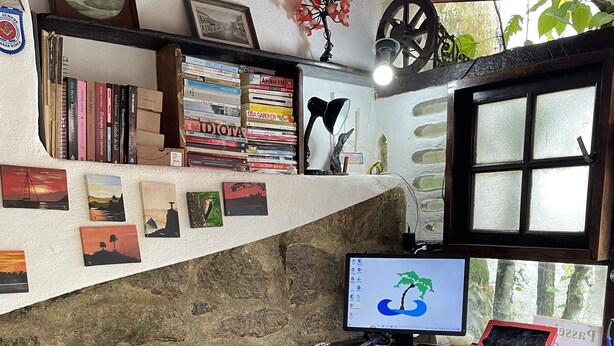 Una oficina rústica con pared de piedra, un escritorio de madera, una computadora y varios libros y cuadros.
