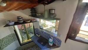 Cocina compacta con un lavamanos pequeño, cafetera y ventana con vistas al exterior.