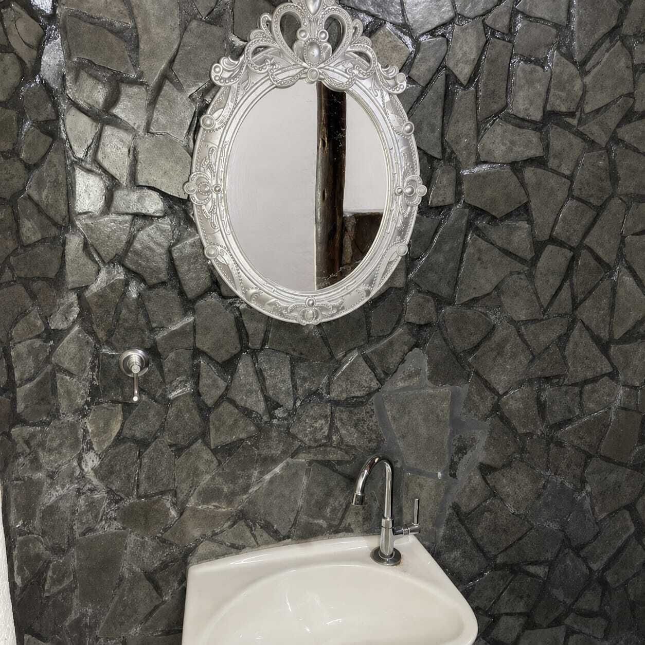 A bathroom with a stone mosaic wall, a white sink, and a decorative mirror.