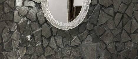 A bathroom with a stone mosaic wall, a white sink, and a decorative mirror.