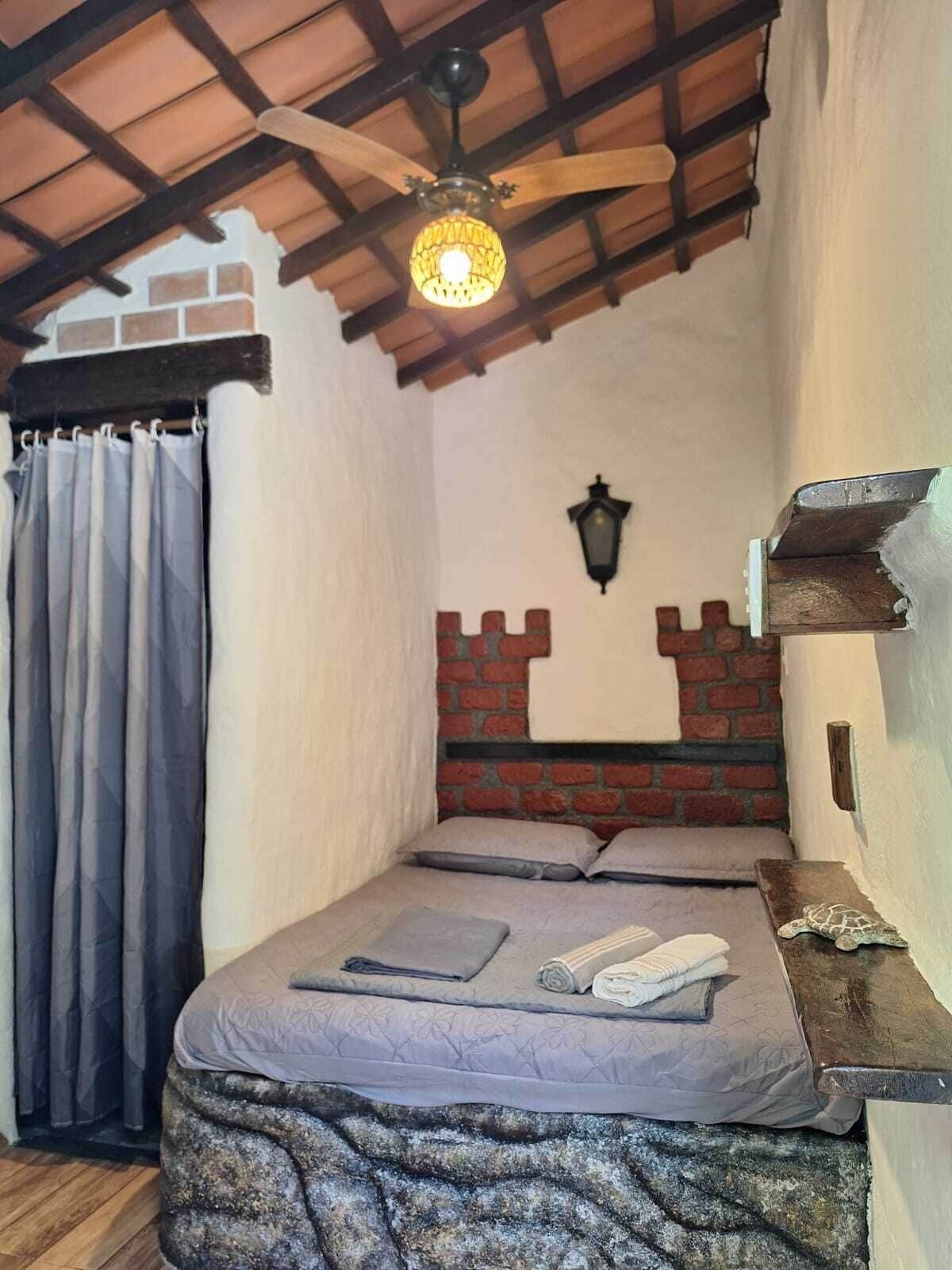 Une chambre avec un lit, une tête de lit en bois, un mur d’accent en briques, un luminaire fixé au mur et un rideau.