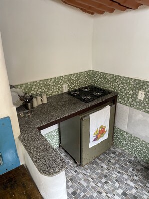 Une cuisine de taille réduite, équipée d’une cuisinière à gaz, d’un évier et d’un plan de travail recouvert de carreaux.