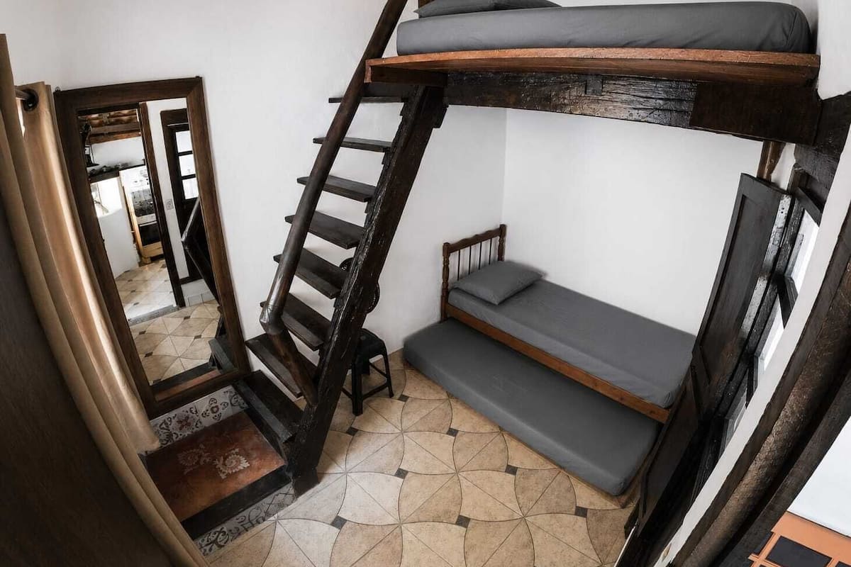 A bunk bed with a ladder, a small seating area, and a patterned floor.