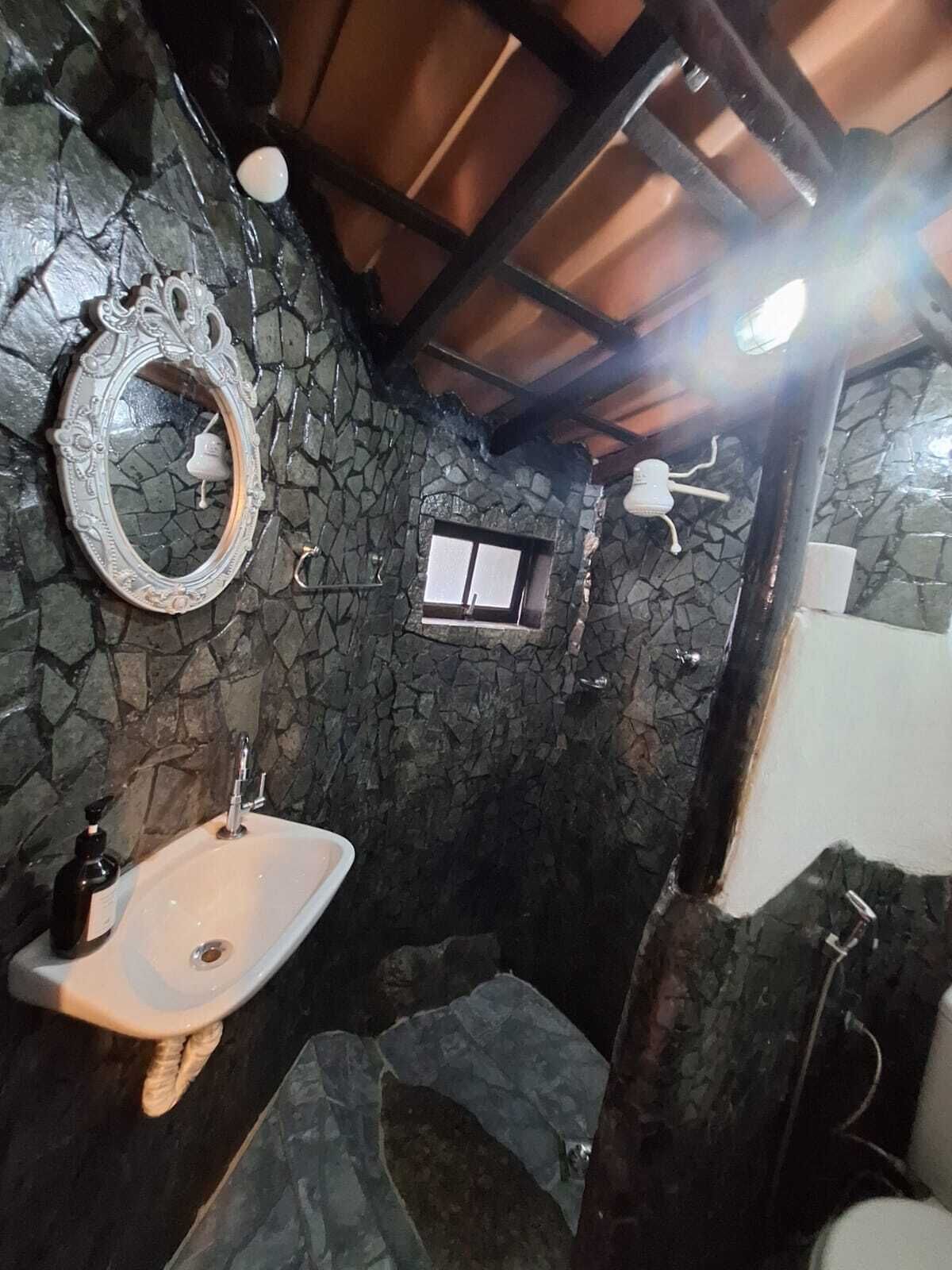 Een badkamer met een stenen muur, een wit wastafelmeubel, een spiegel en een klein raam.