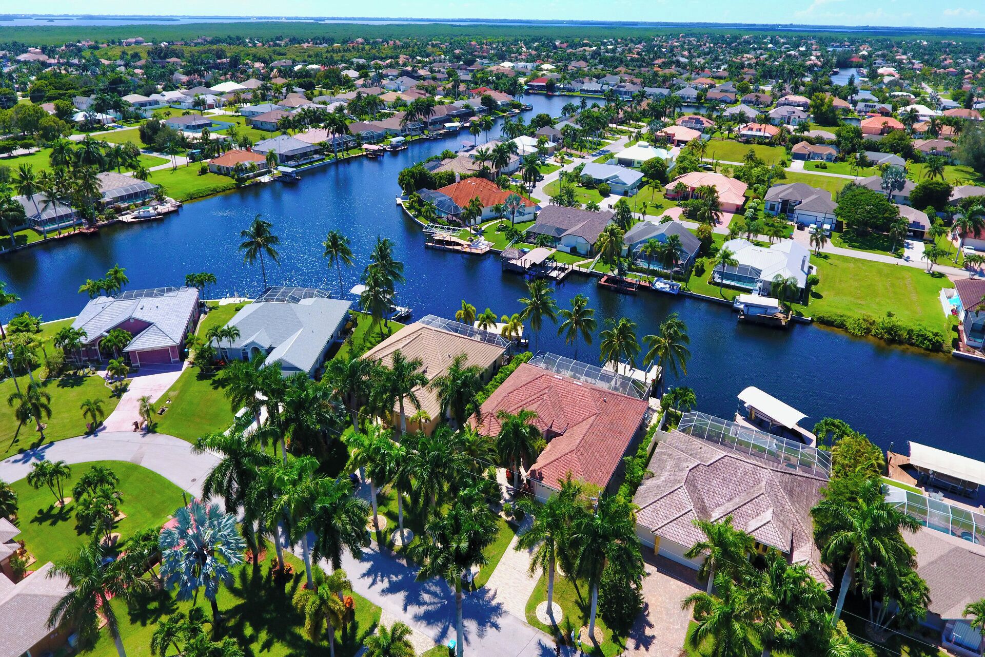 An aerial view of a residential area with houses, a river, and palm trees.