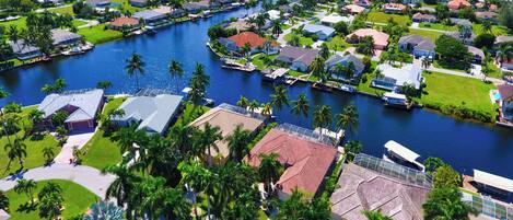 An aerial view of a residential area with houses, a river, and palm trees.