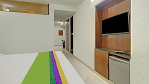 A hotel room with a bed, a TV mounted on a wooden cabinet, and a small kitchenette area. - Treebo Sky 5 (Panchkula)