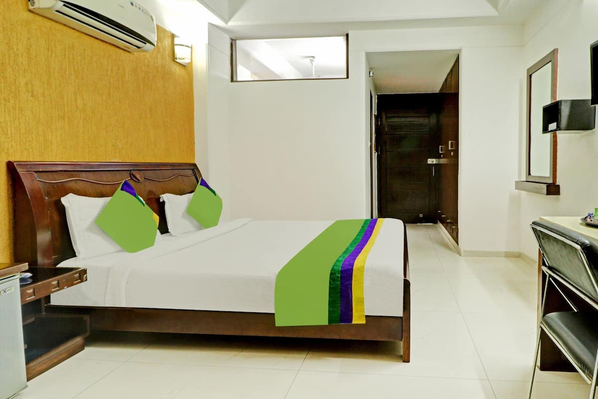 Quarto de hotel com cama de madeira, uma secretária pequena, televisão de tela plana e porta que dá para outro quarto.