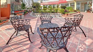 A courtyard with ornate metal chairs and tables, surrounded by potted plants and a building with a glass facade. - Treebo Sky 5 (Panchkula)