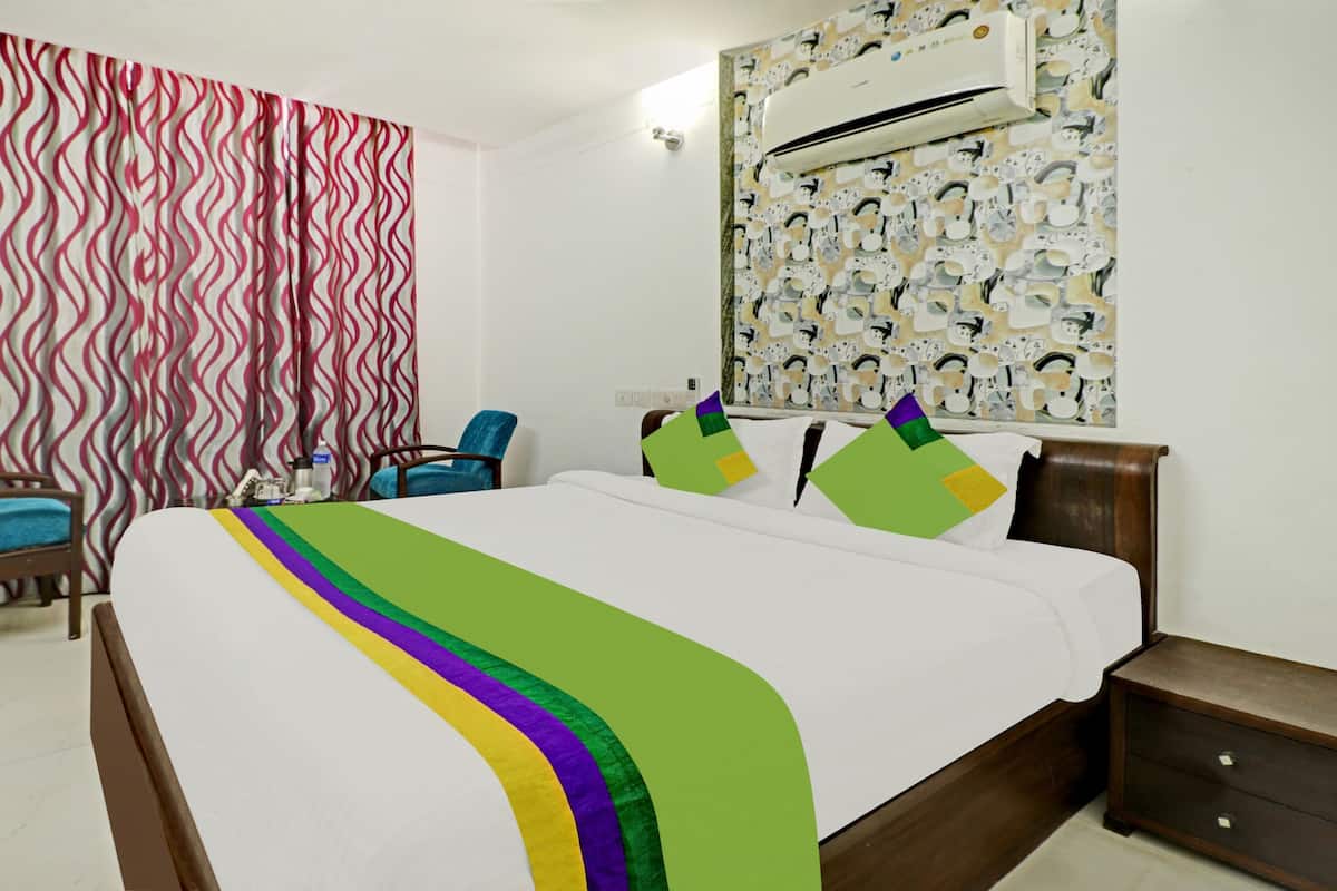 Quarto de hotel com cama, poltrona, mesa de cabeceira, ar condicionado e cortina estampada.