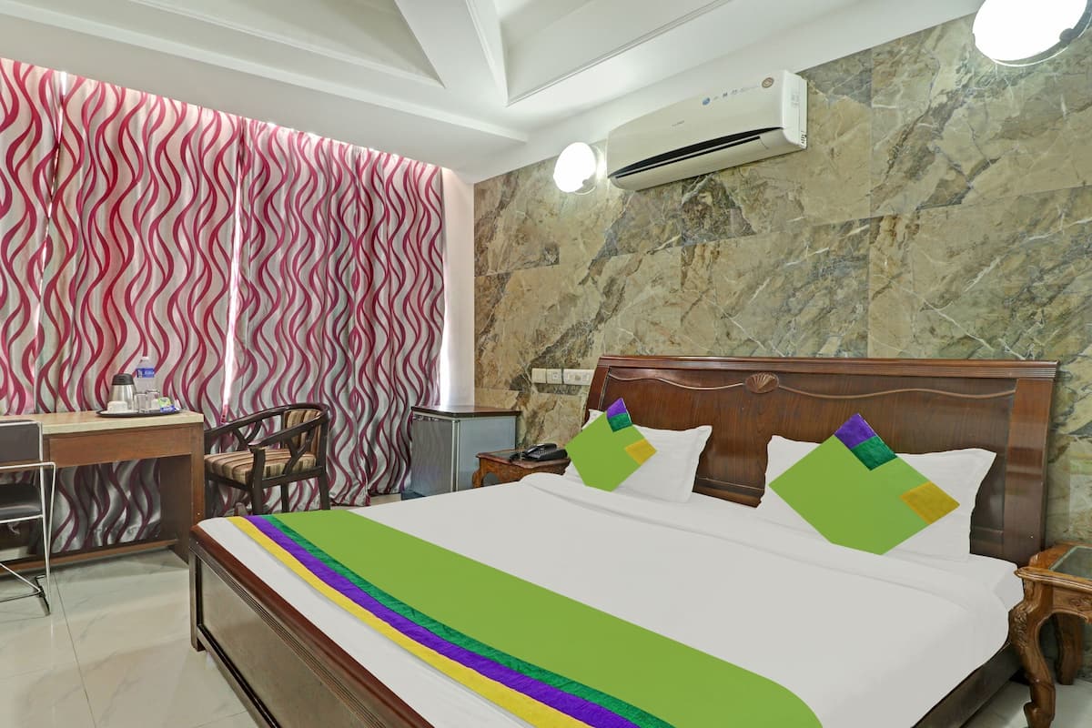 Quarto de hotel com cama, escrivaninha, cadeira, ar condicionado e parede de mármore.