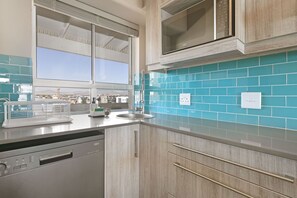 A modern kitchen with a dishwasher, a microwave, and a window with a view of a construction site. - Sea Spray B404 by HostAgents (Cape Town)